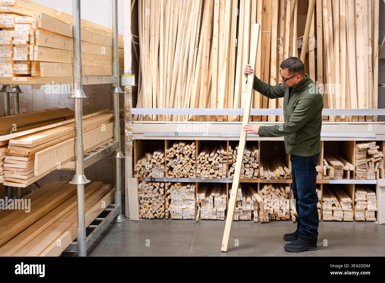 Man selecting timber (wooden bar) for DIY project. Man seller checking quality of lumber board in hardware store or wood warehouse. Stock Photo