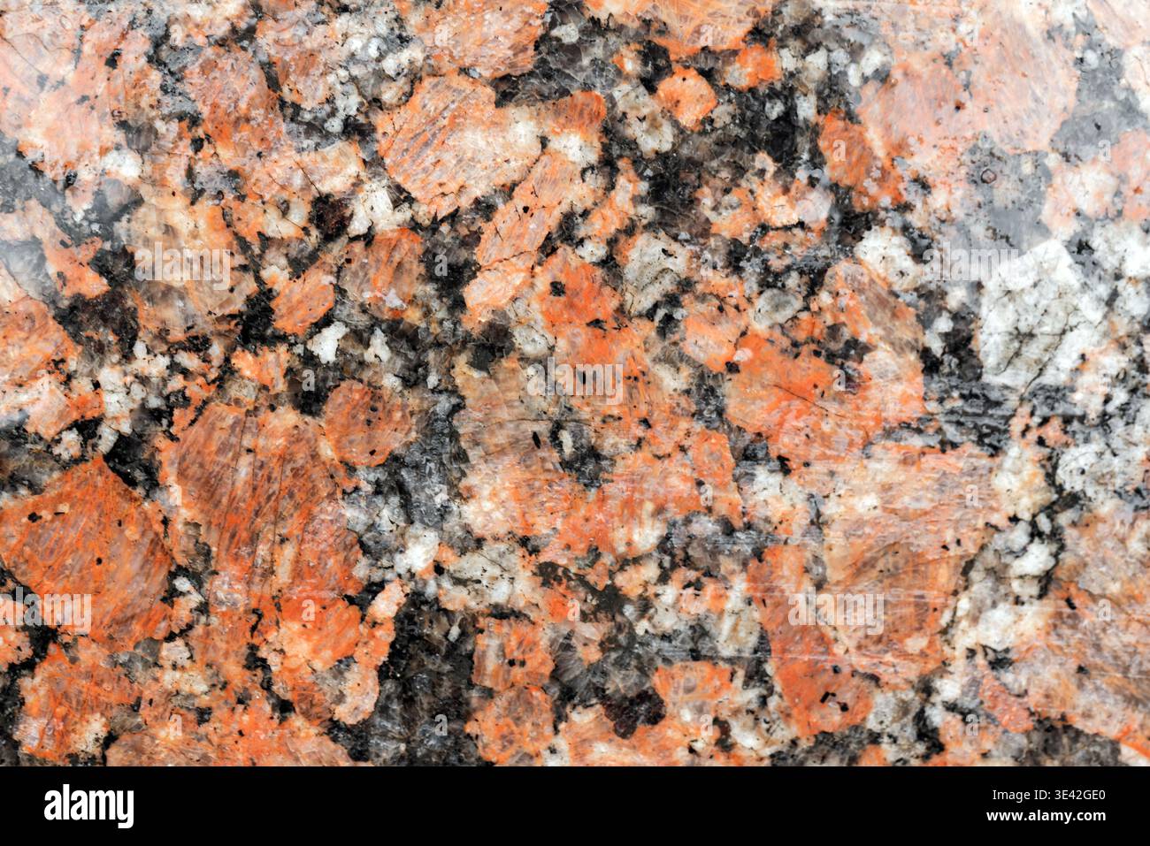 Polished red granite close-up showing speckled black, white and pink crystals. Natural stone texture ideal for countertops, flooring, wall cladding, a Stock Photo