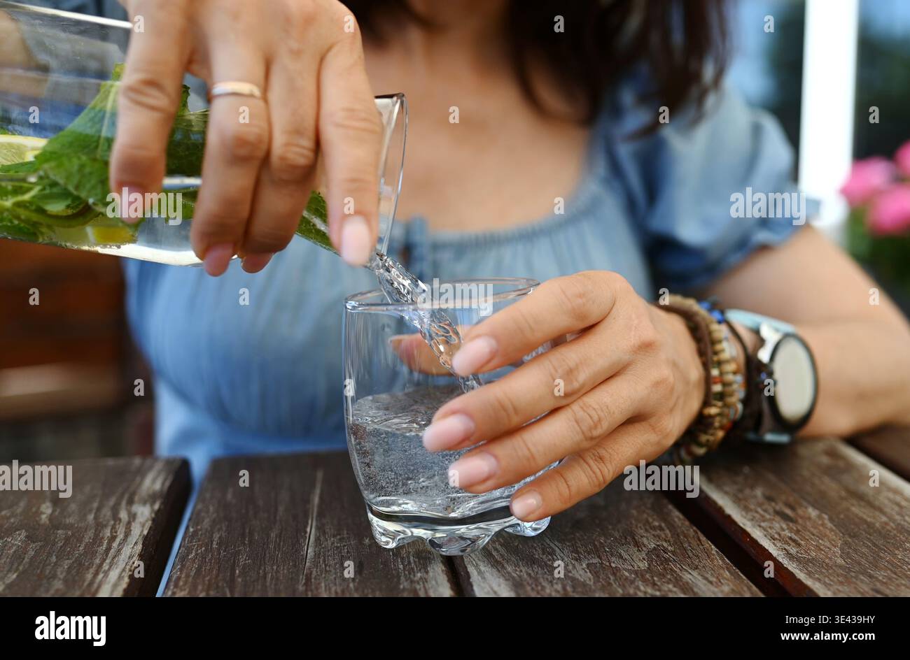 Girl Sitting In An Open-Air Cafe Pouring Fresh Water With Mint And Lemon Into A Glass Stock Photo