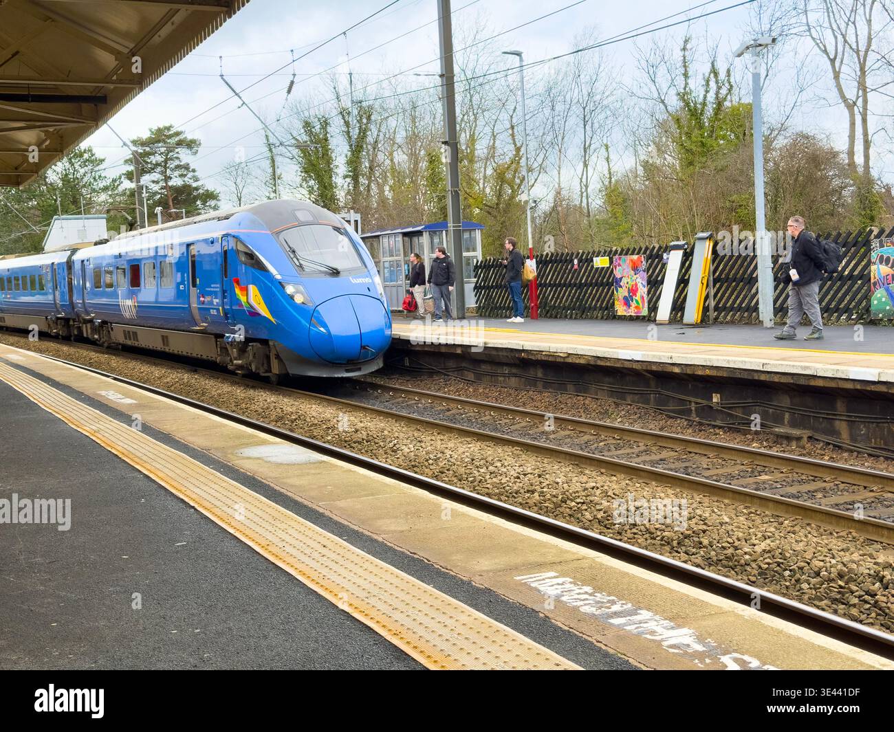 A blue Lumo train Class 803 unit 803003 arriving at Morpeth station platform UK with a passenger waiting by the tracks East Coast Main Line - Smartphone Captured Stock Image