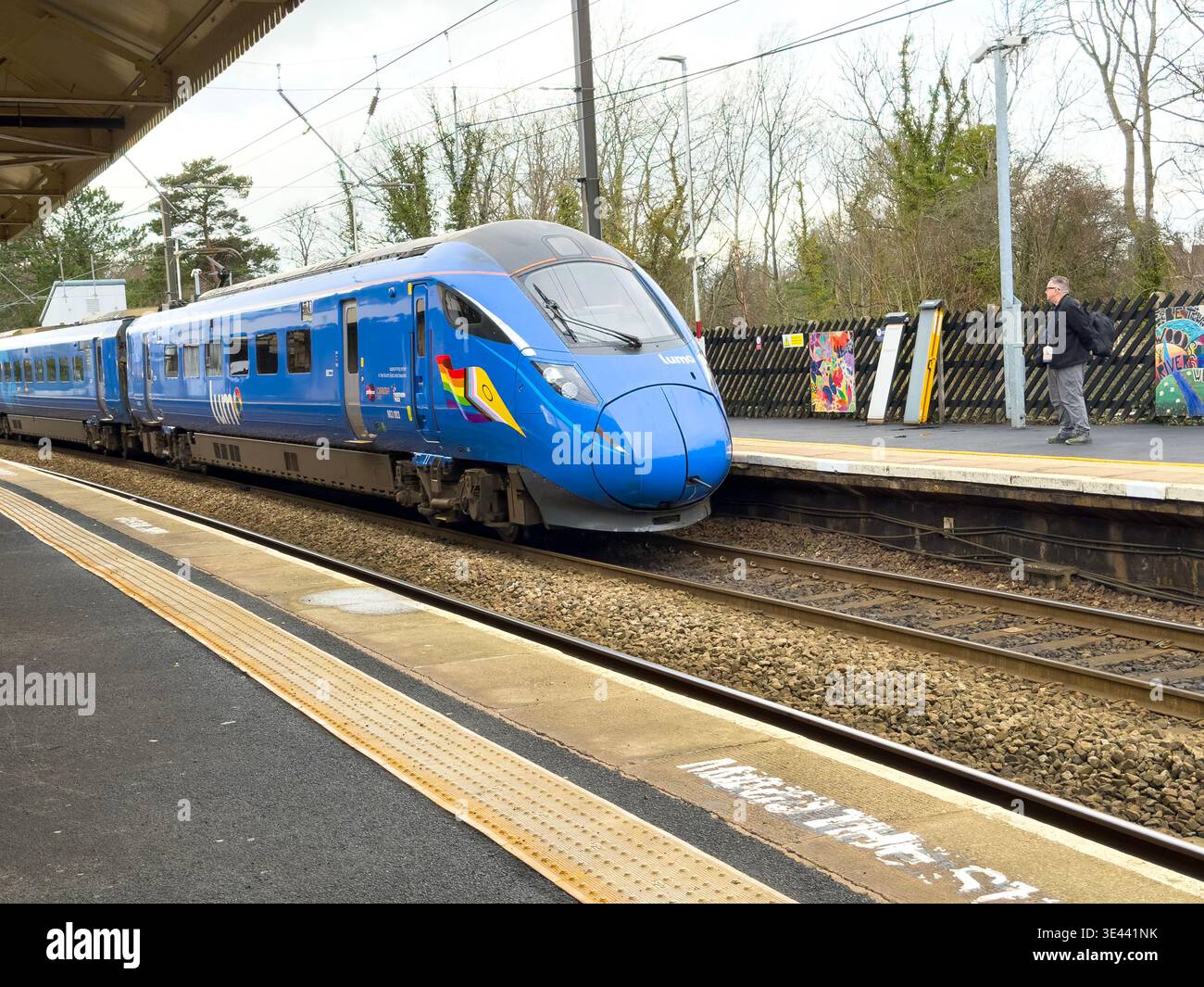 A blue Lumo train Class 803 unit 803003 arriving at Morpeth station platform UK with a passenger waiting by the tracks East Coast Main Line - Smartphone Captured Stock Image