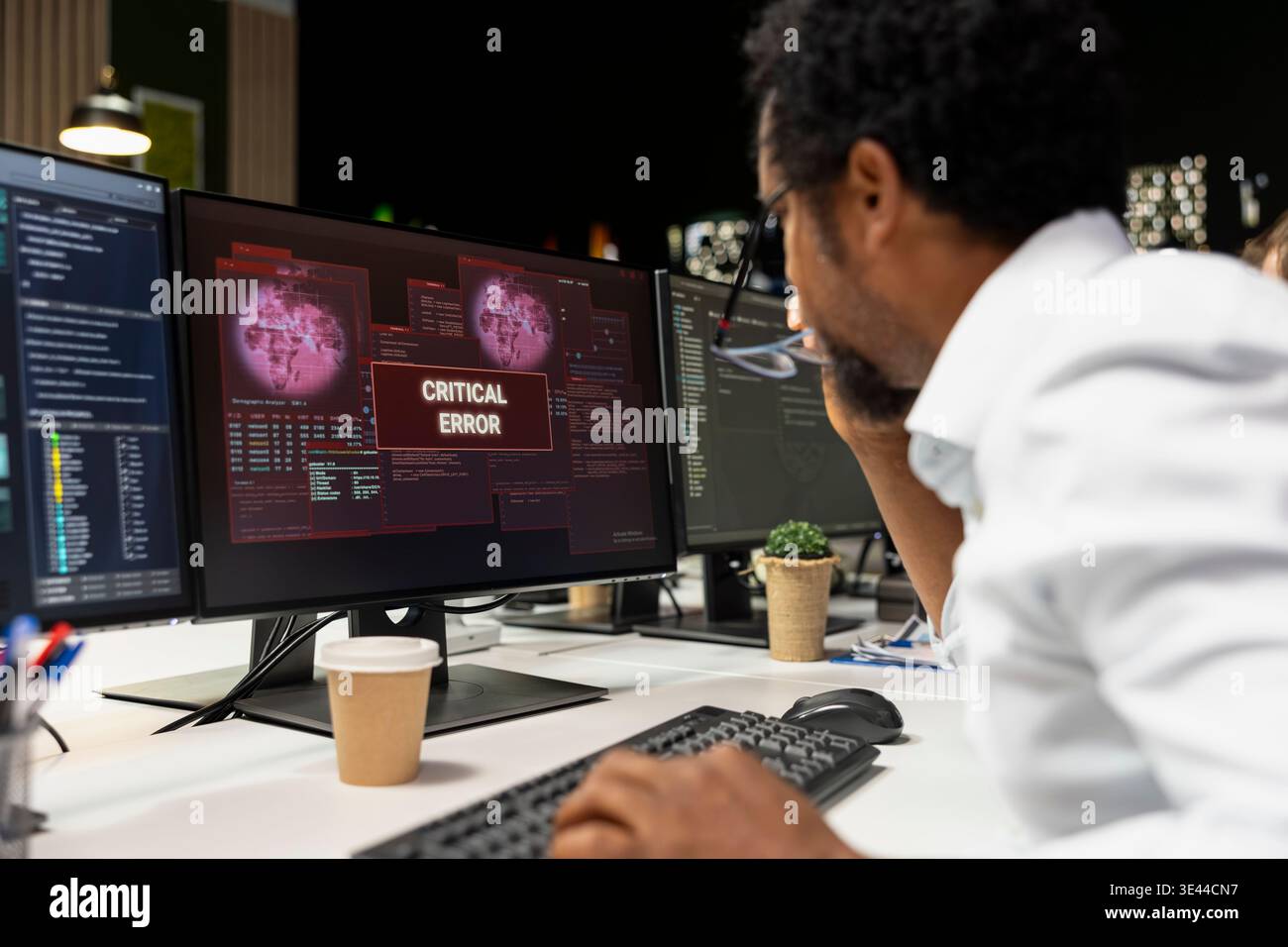 Technician at office desk thinking how to fix critical error warning displayed on PC monitor. African american man in tech startup brainstorming how to fix computer bug affecting server network Stock Photo