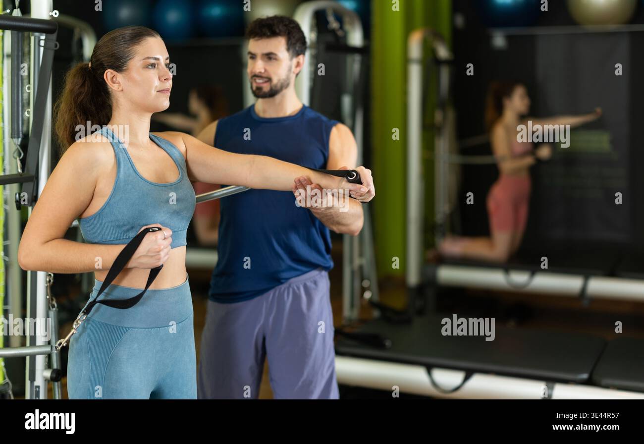 Young woman doing arm exercises and male trainer helping her Stock Photo