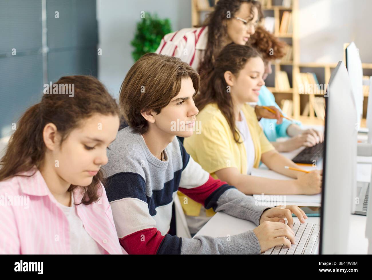 Focused teens and teacher working on computers in collaborative coding class Stock Photo