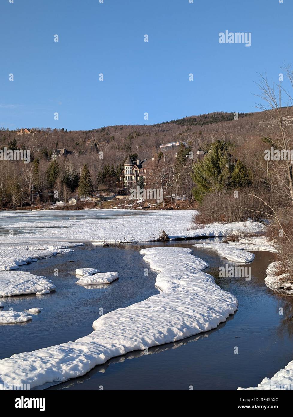 Thaw on a lake in spring on a beautiful spring day, the lake shore is surrounded by trees and estates, water breaks through the snow and ice, mountain - Smartphone Captured Stock Image
