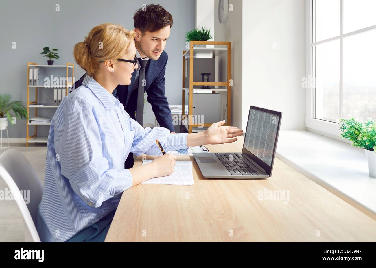 Two colleagues work in office on joint project and analyze data and plan together using laptop. Stock Photo