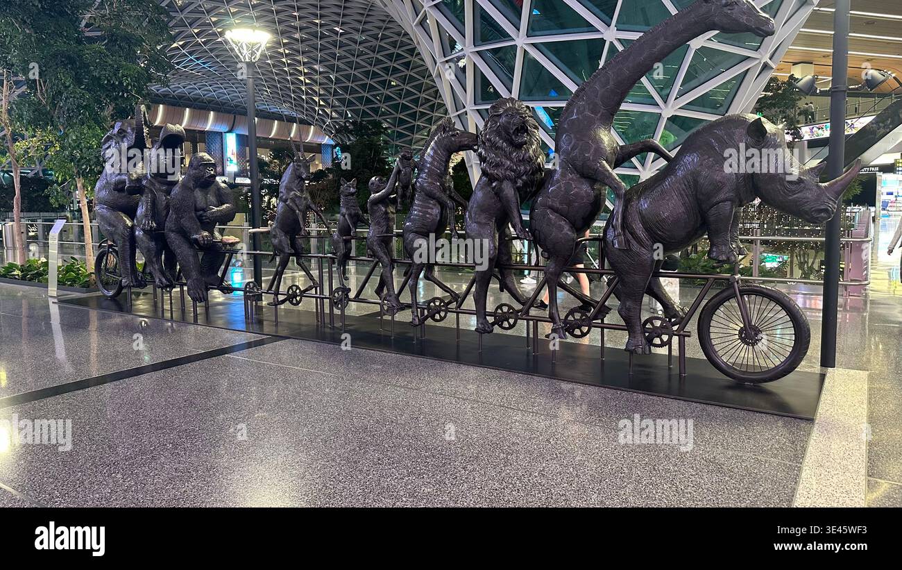 Creative indoor sculpture showing multiple animals riding a bicycle inside a modern airport terminal with glass and steel structure. - Smartphone Captured Stock Image
