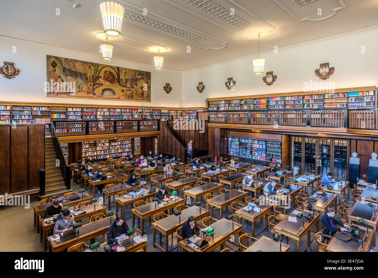 The first reading room at the German National Library in Leipzig, featuring green reading lamps and a green linoleum work surface. The walls are adorned with frescoes depicting Late Nazarene motifs. Leipzig, Saxony, Germany Stock Photo