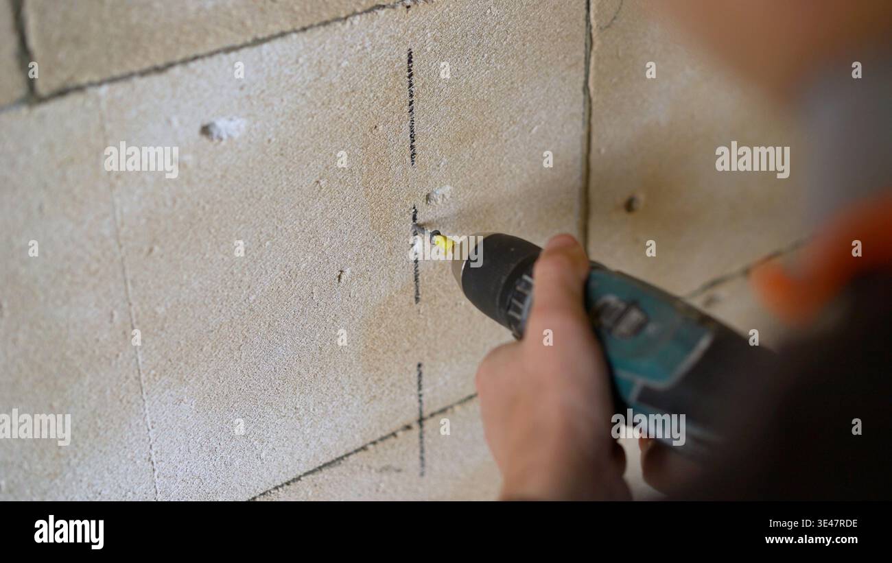 Worker using a cordless power drill to make a hole in a block wall. Stock Photo