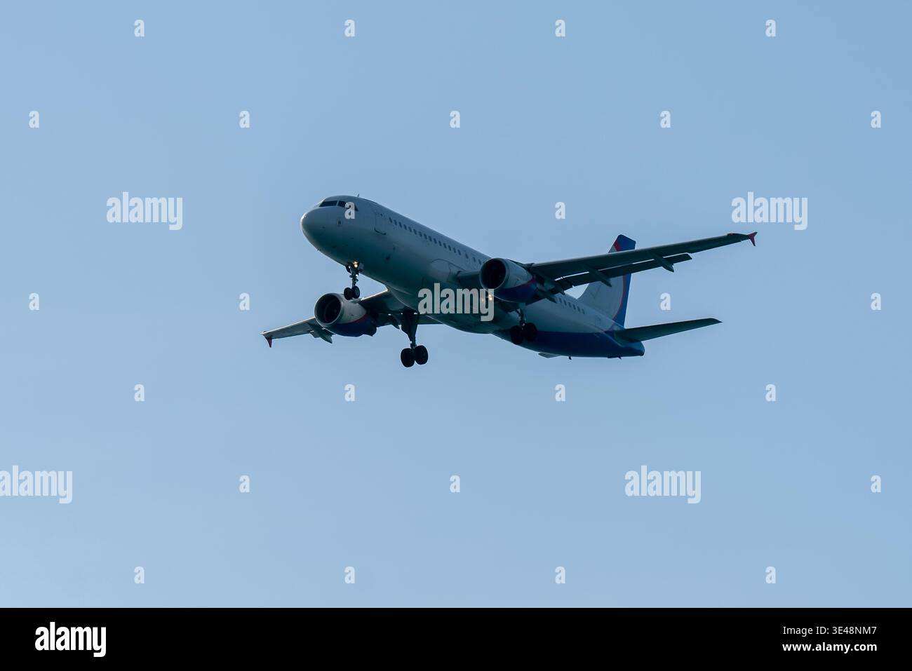 Commercial airliner descends with landing gear extended against a clear blue sky during final approach, illustrating modern aviation, passenger travel Stock Photo