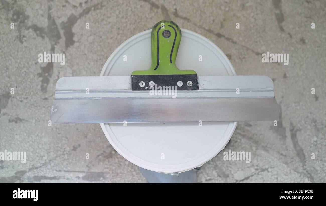 Construction worker using notched trowel and bucket for applying plaster during renovation Stock Photo