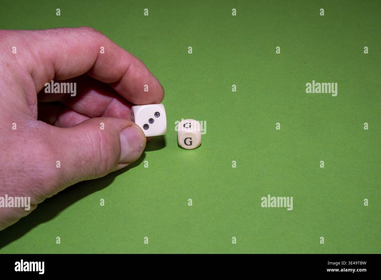 Hand holding a white dice, another on a green background Stock Photo