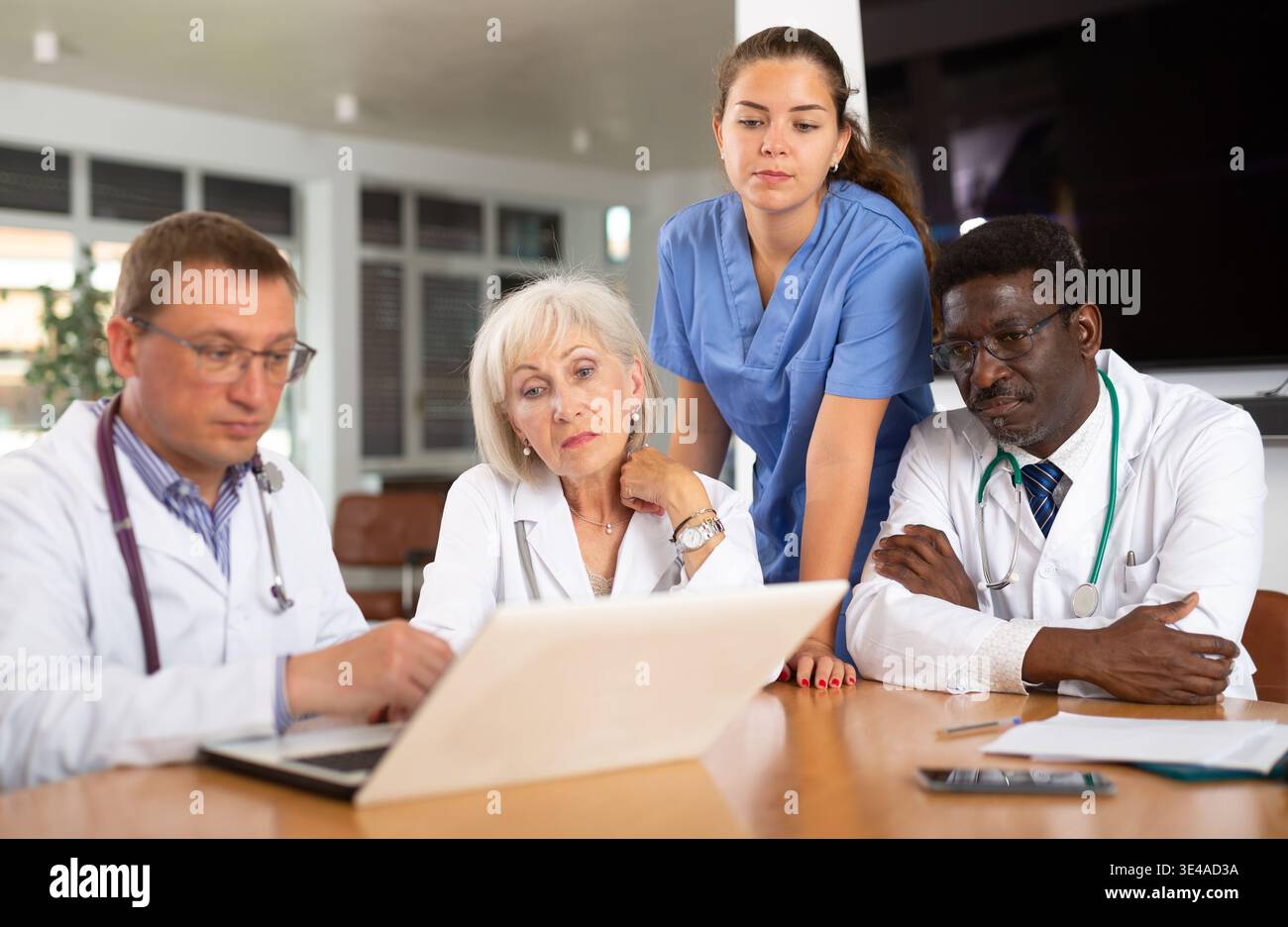Doctors sitting around the table looking at the notebook Stock Photo