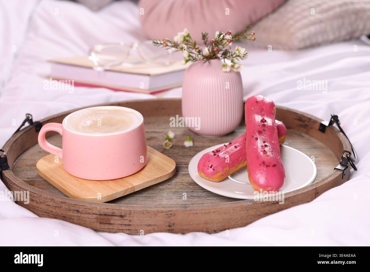 Aromatic coffee in cup, eclairs, and beautiful flowers on bed, closeup Stock Photo
