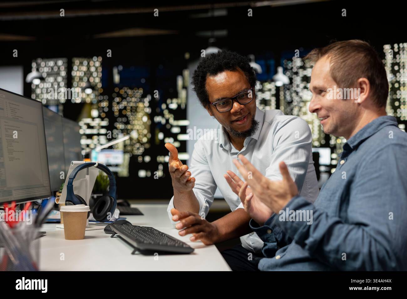 Upbeat programmers laughing, sharing jokes in startup office while optimizing code for performance and scalability. Jolly coworkers talking while using programming languages on computer Stock Photo