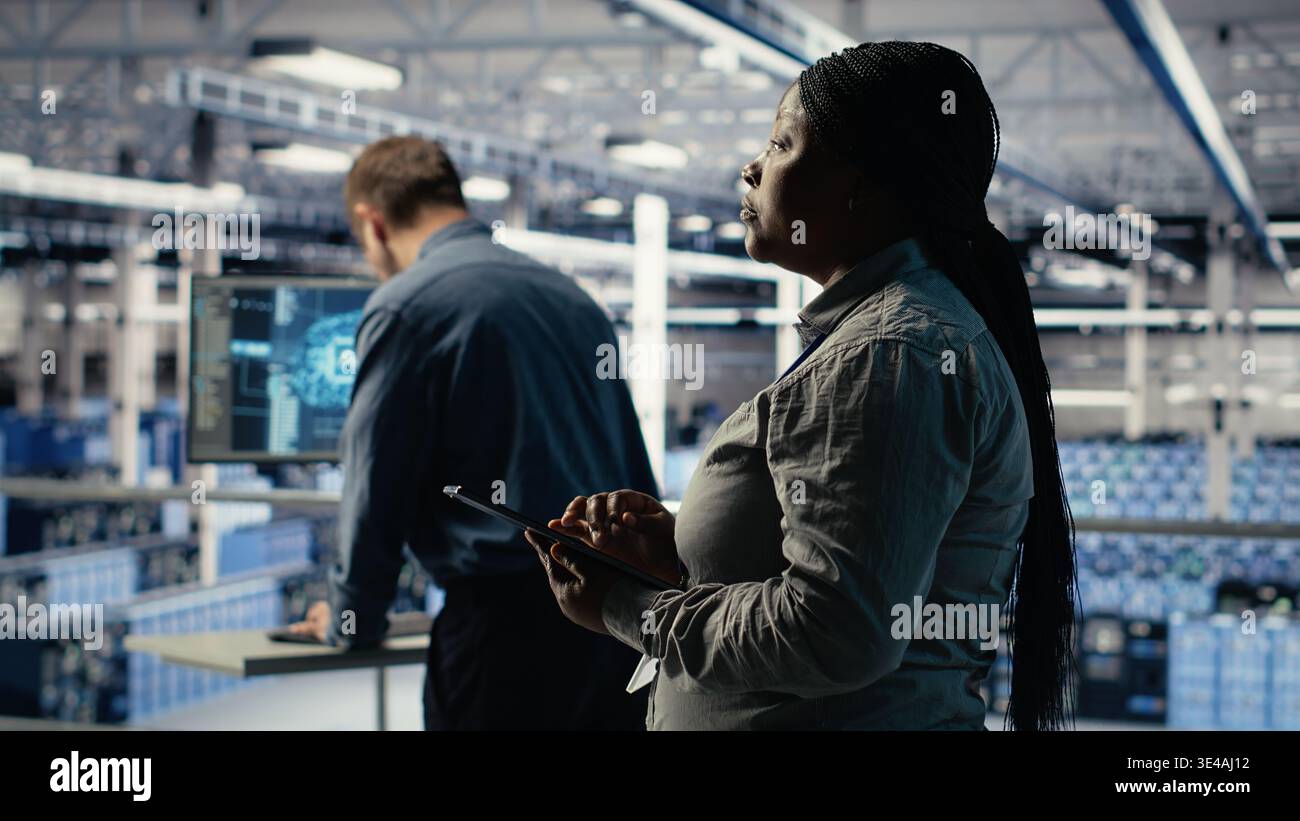 Teamworking data center programmers investigate neural networks configuration, making adjustments for optimal function. Server hub colleagues work together to check deep learning errors, camera B Stock Photo
