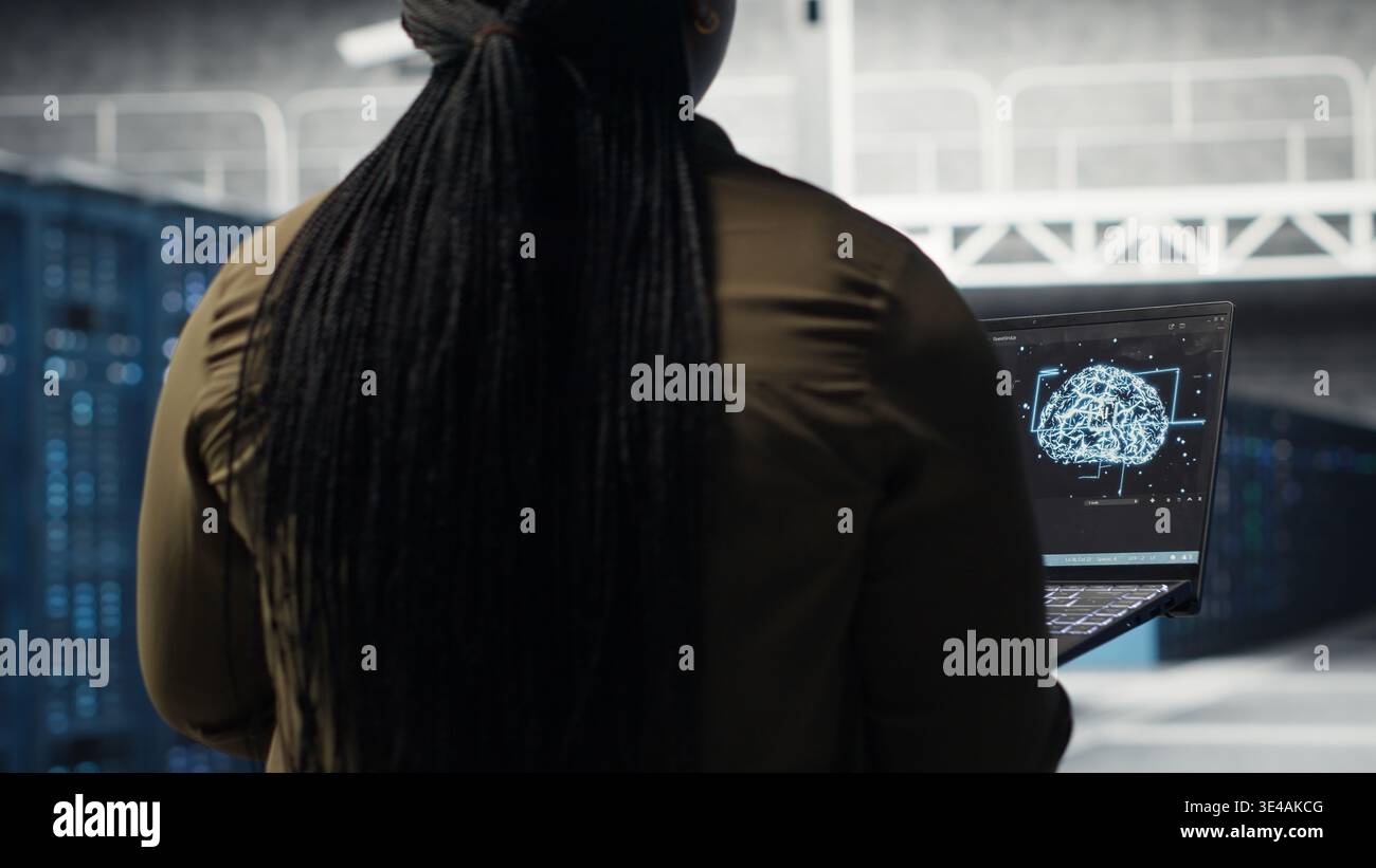 Computer scientist doing data center automation using AI on laptop. Server room IT specialist implements machine learning driven predictive maintenance systems using notebook, camera B Stock Photo