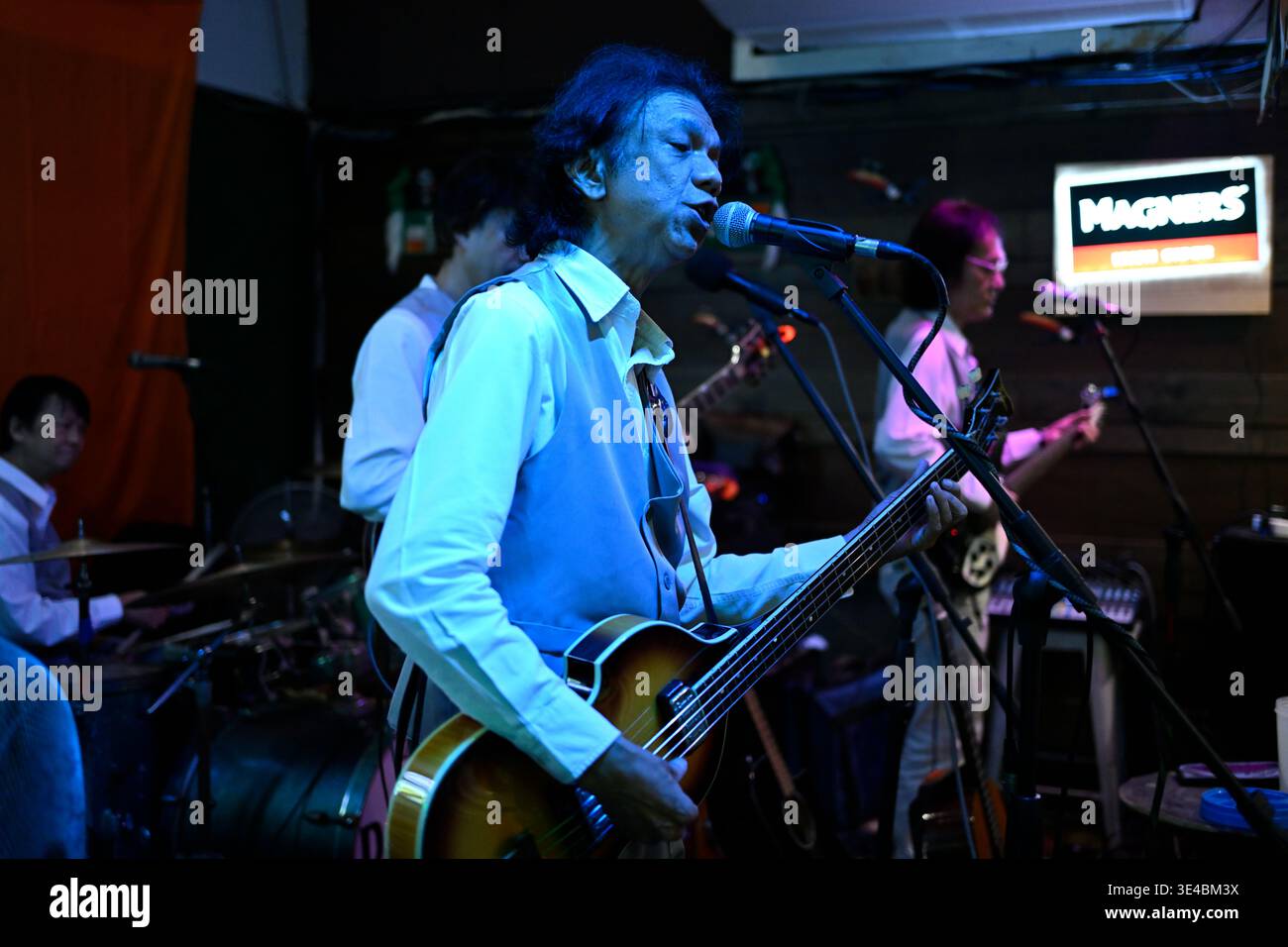 A right-handed "Paul McCartney" performs live with the tribute band The Bangkok Beatles in Hua Hin, Thailand. Stock Photo