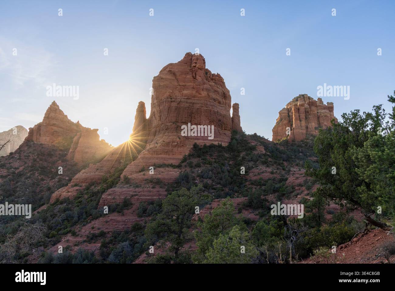 Starburst sun setting behind red rock formations Stock Photo
