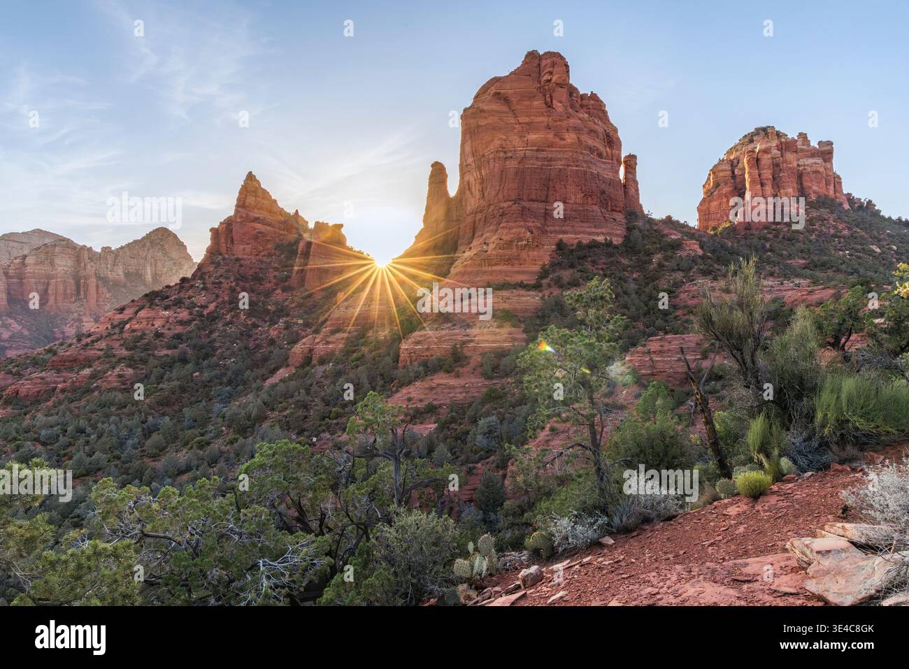 Starburst sun setting behind red rock landscape Stock Photo