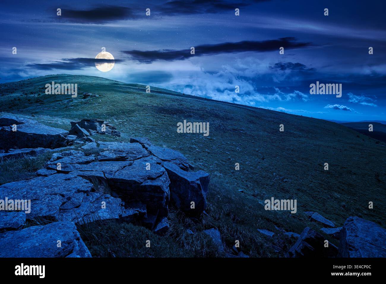 rocks and rolling hills in mountain landscape in summer at night. full moon over scenery with green grass on alpine meadow under dark sky with clouds. Stock Photo