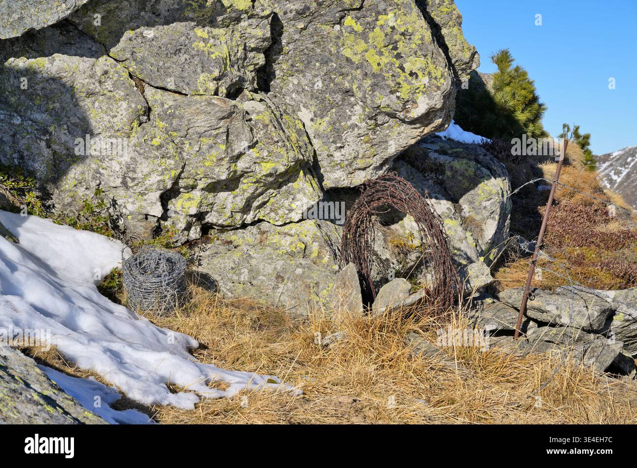 Coiled rusty barbed wire in a rugged mountain landscape. Stock Photo