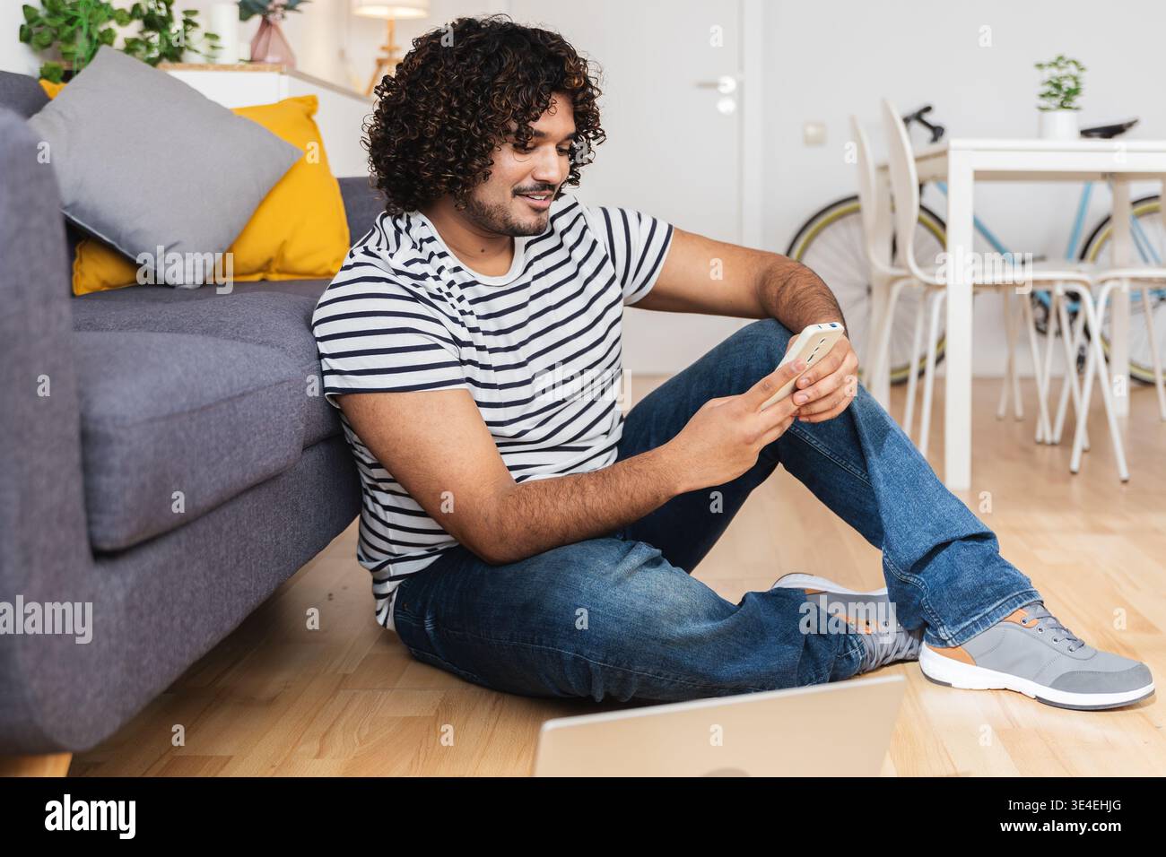 Young Indian man sitting on floor using phone Stock Photo