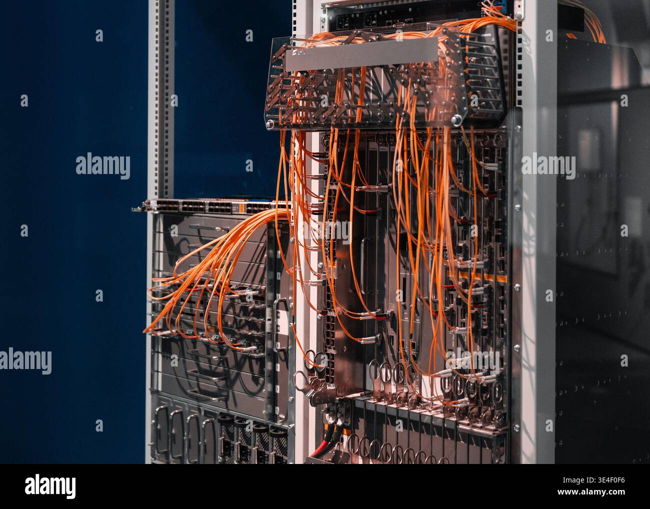 Two server racks with orange cables. Data center's core network switch with numerous computers and routers - data center'd high-speed architecture. Stock Photo
