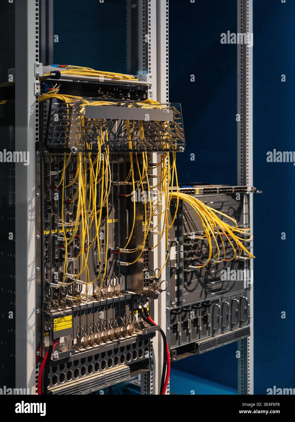 Two server racks with bright yellow cables. Data center's core network switch with numerous computers and routers - high-speed modular architecture. Stock Photo