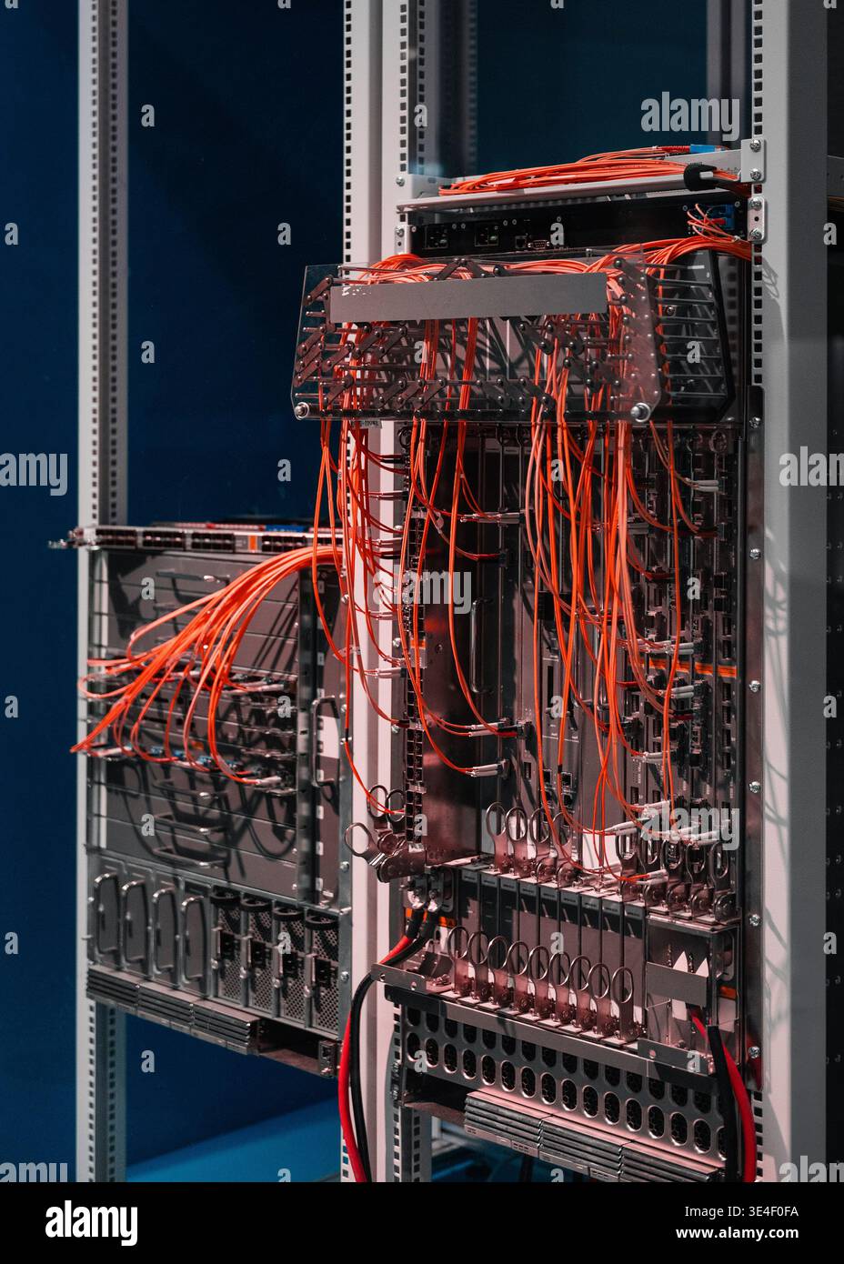 Two server racks with orange cables. Data center's core network switch with numerous computers and routers - high-speed modular architecture. Stock Photo