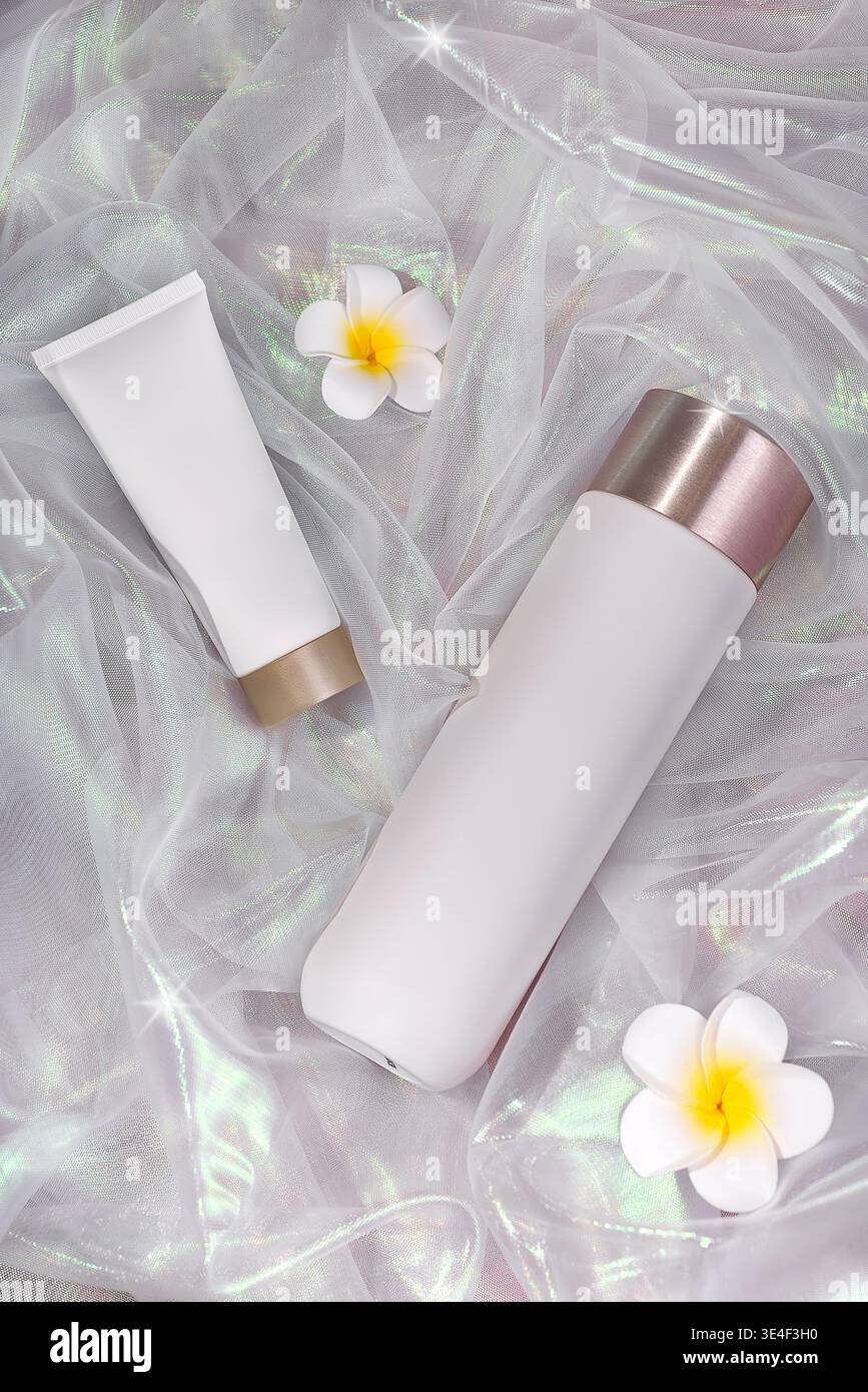 Cosmetic tubes with flowers on iridescent fabric background. Stock Photo