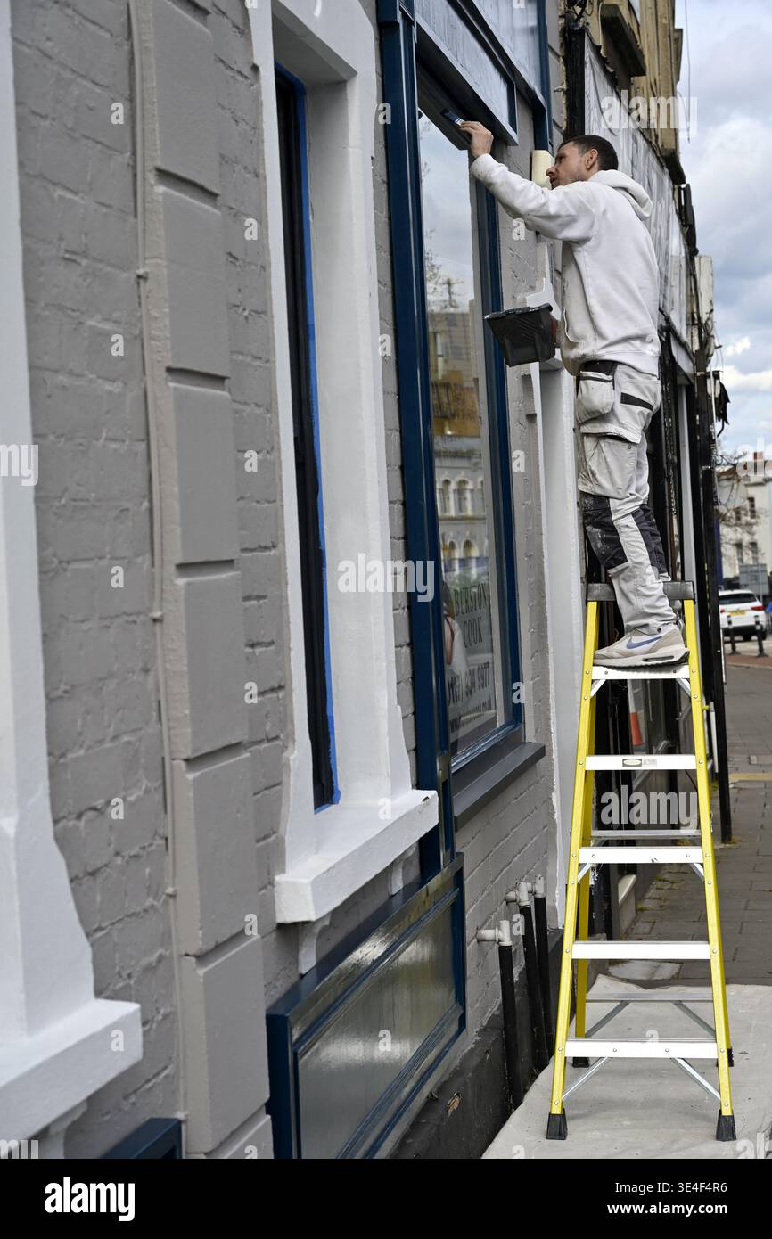 Man on ladder painting the front facade of shop Stock Photo
