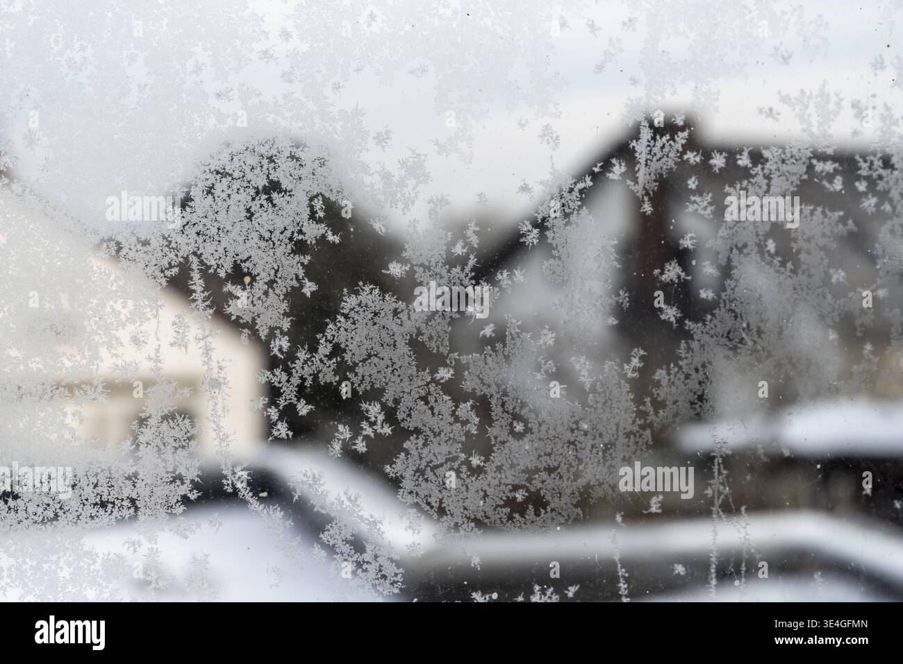 Frozen window glass showing natural frost patterns with blurred winter landscape outside Stock Photo