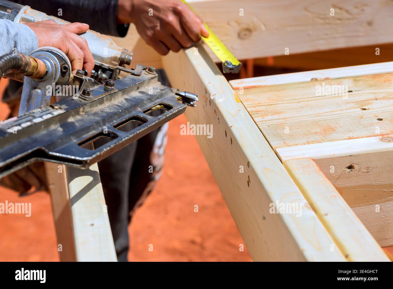 Worker cuts wood using saw while measuring with tape in construction site Stock Photo