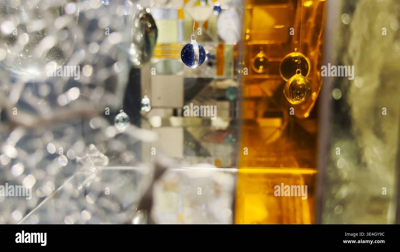 Abstract glass installation with suspended spheres and mirrored surfaces. Light reflections and refractions create layered shapes, depth, and a Stock Photo