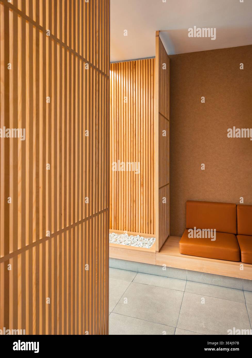 A modern interior space featuring vertical wooden slats and a comfortable brown leather sofa, with a minimalist design and natural elements, creating Stock Photo