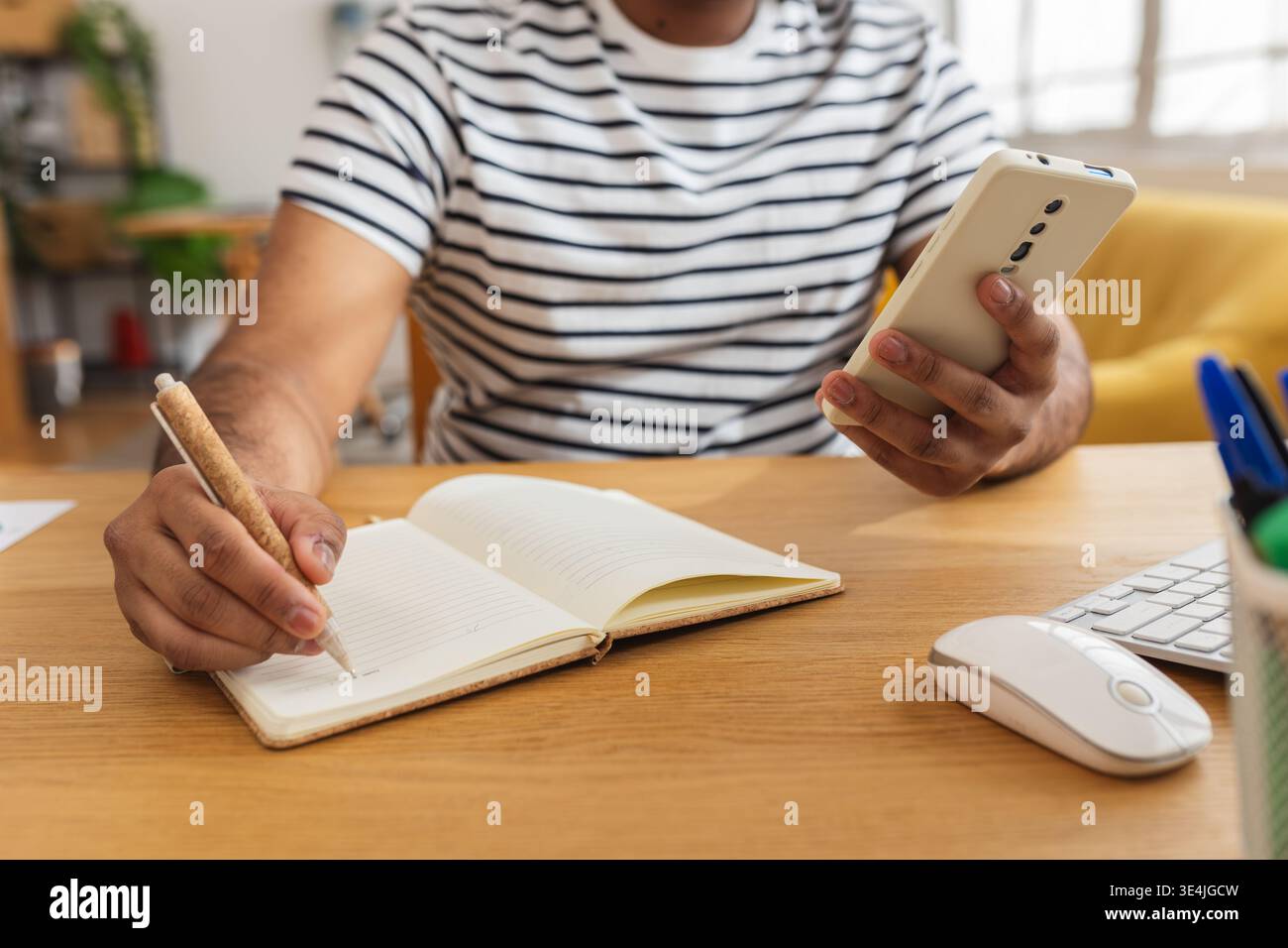 Young Indian man using mobile phone and writing notes Stock Photo