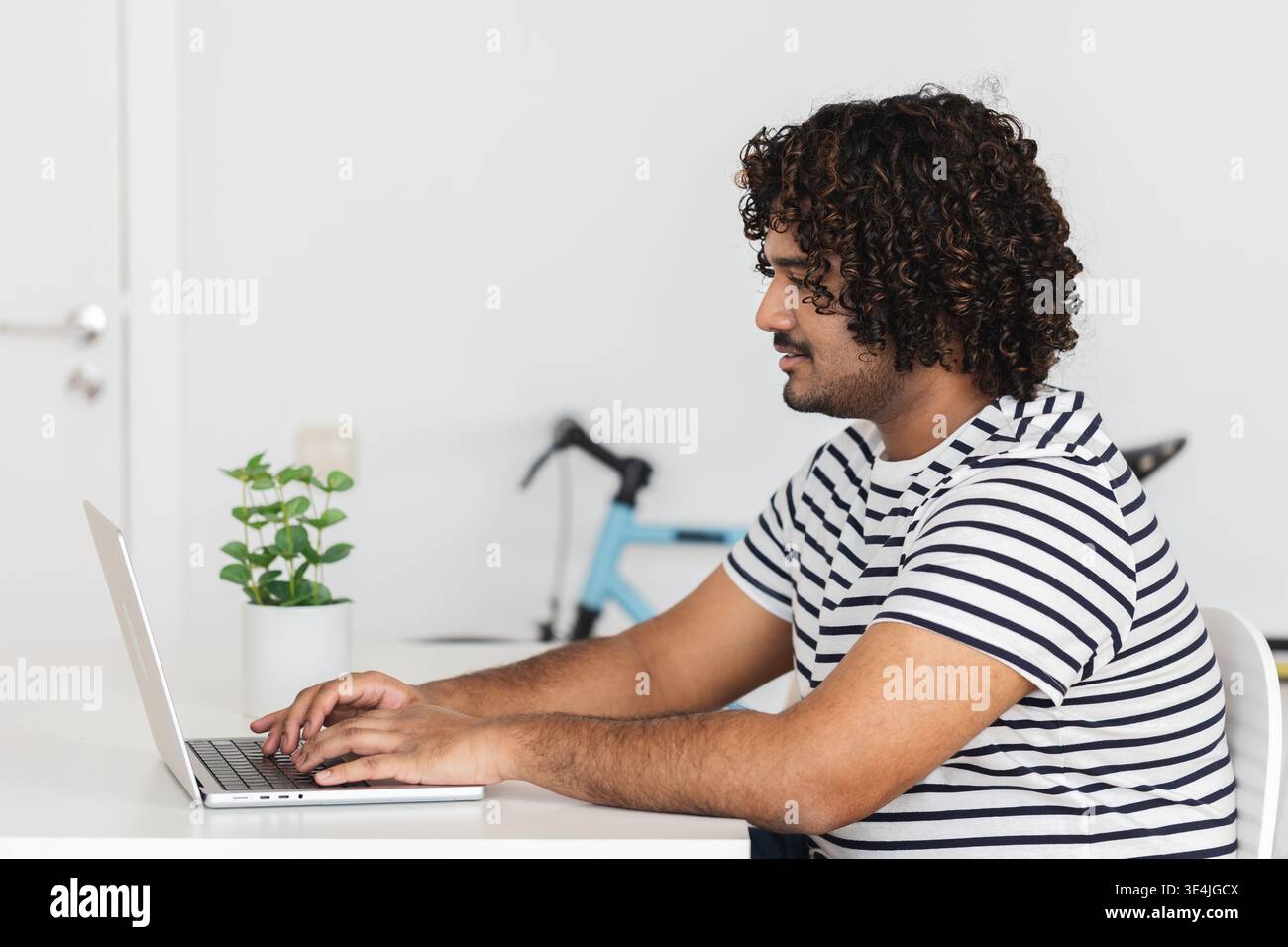Young Indian man typing on laptop side view Stock Photo