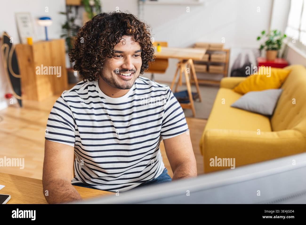Young Indian man working on desktop PC while studying at desk Stock Photo