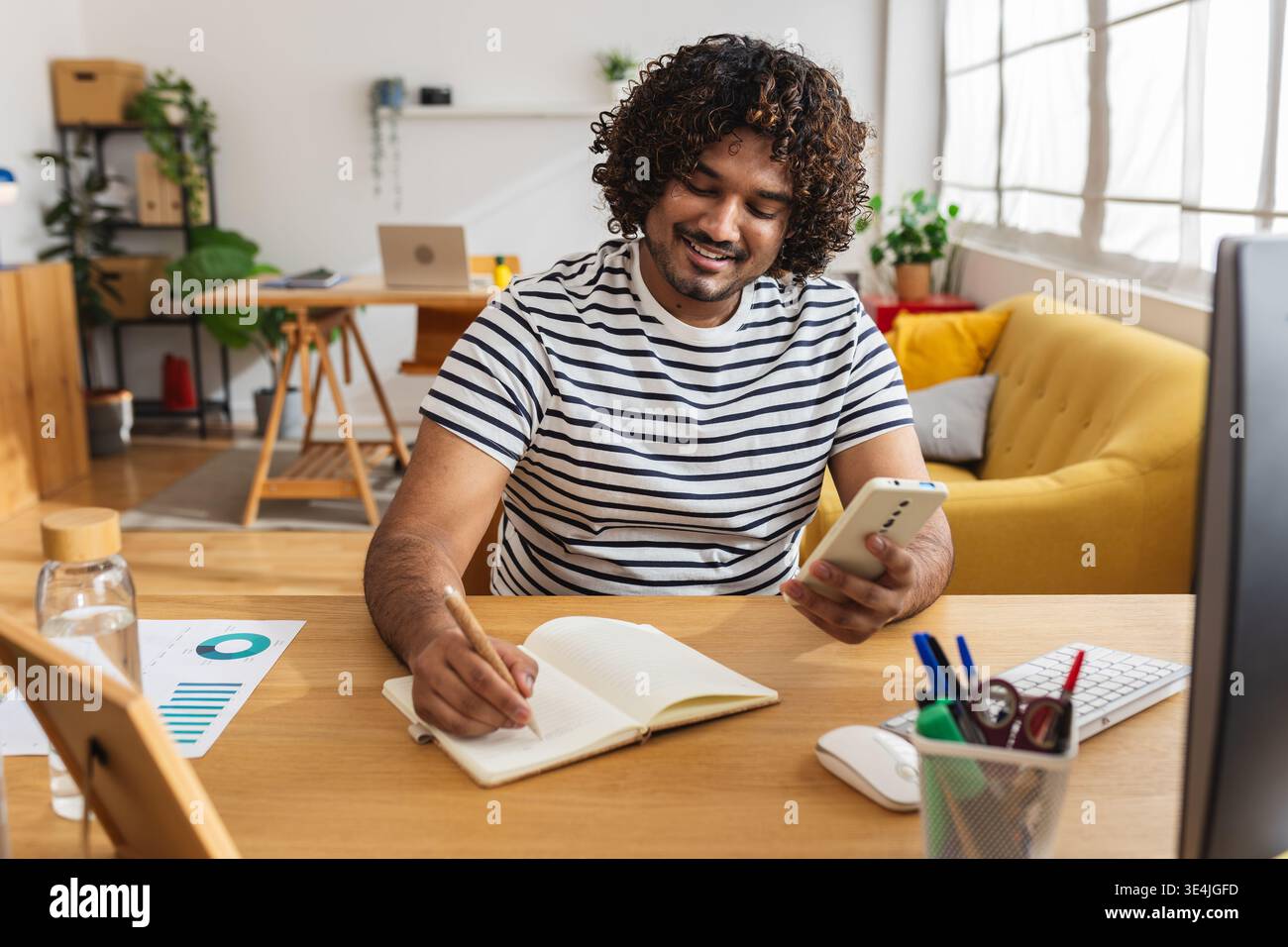 Young Indian man writing notes and checking phone Stock Photo