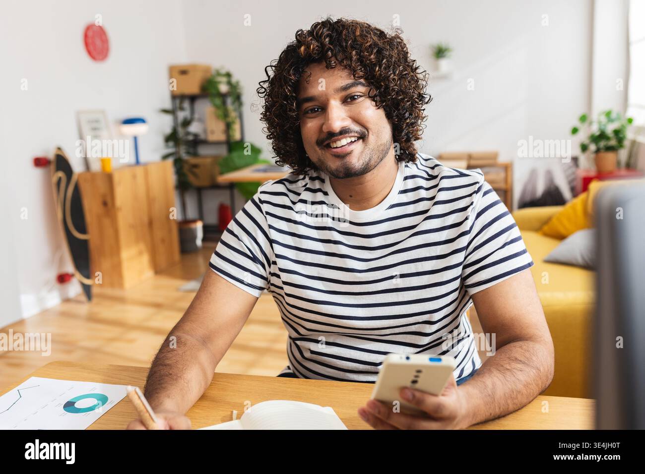Young Indian man holding smartphone and notebook Stock Photo