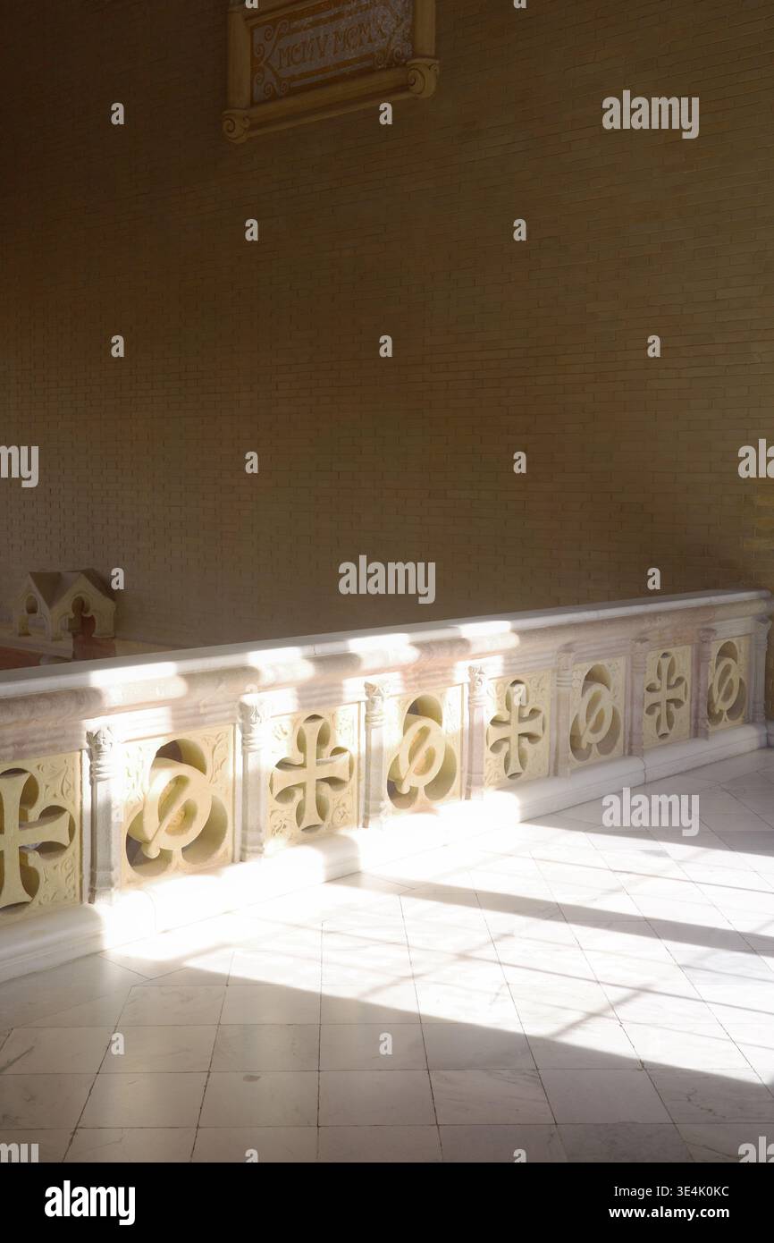 Sunlit carved stone balustrade with cross and quatrefoil motifs casting geometric shadows on white marble floor inside Recinte Modernista de Sant Pau Stock Photo