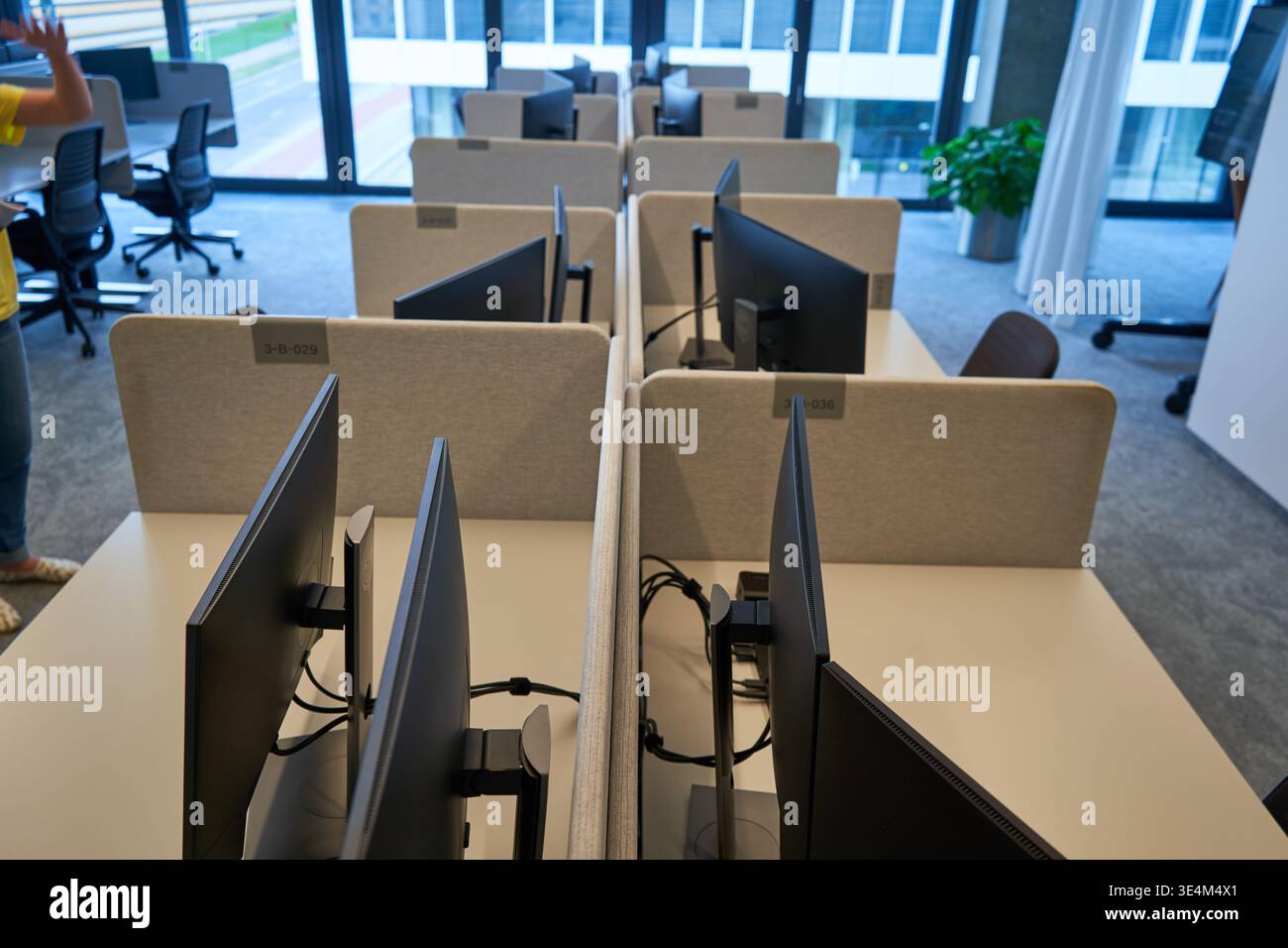 A modern office interior featuring multiple empty workstations arranged in parallel rows. Each desk is equipped with computer monitors mounted on Stock Photo