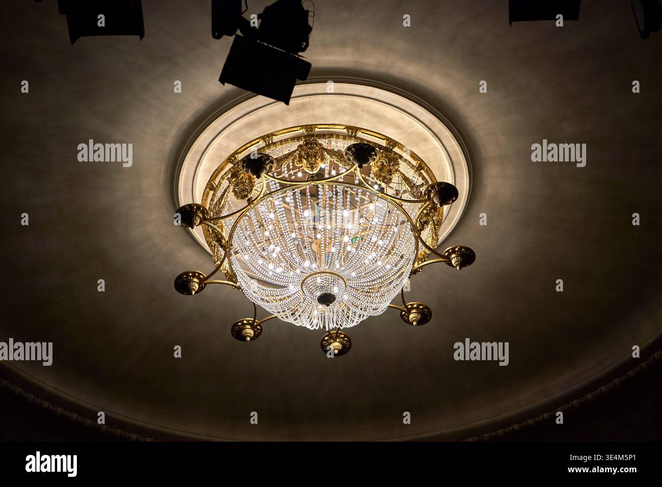 A low-angle view of an ornate crystal chandelier suspended from a domed ceiling. The chandelier features elaborate gold or brass metalwork with Stock Photo