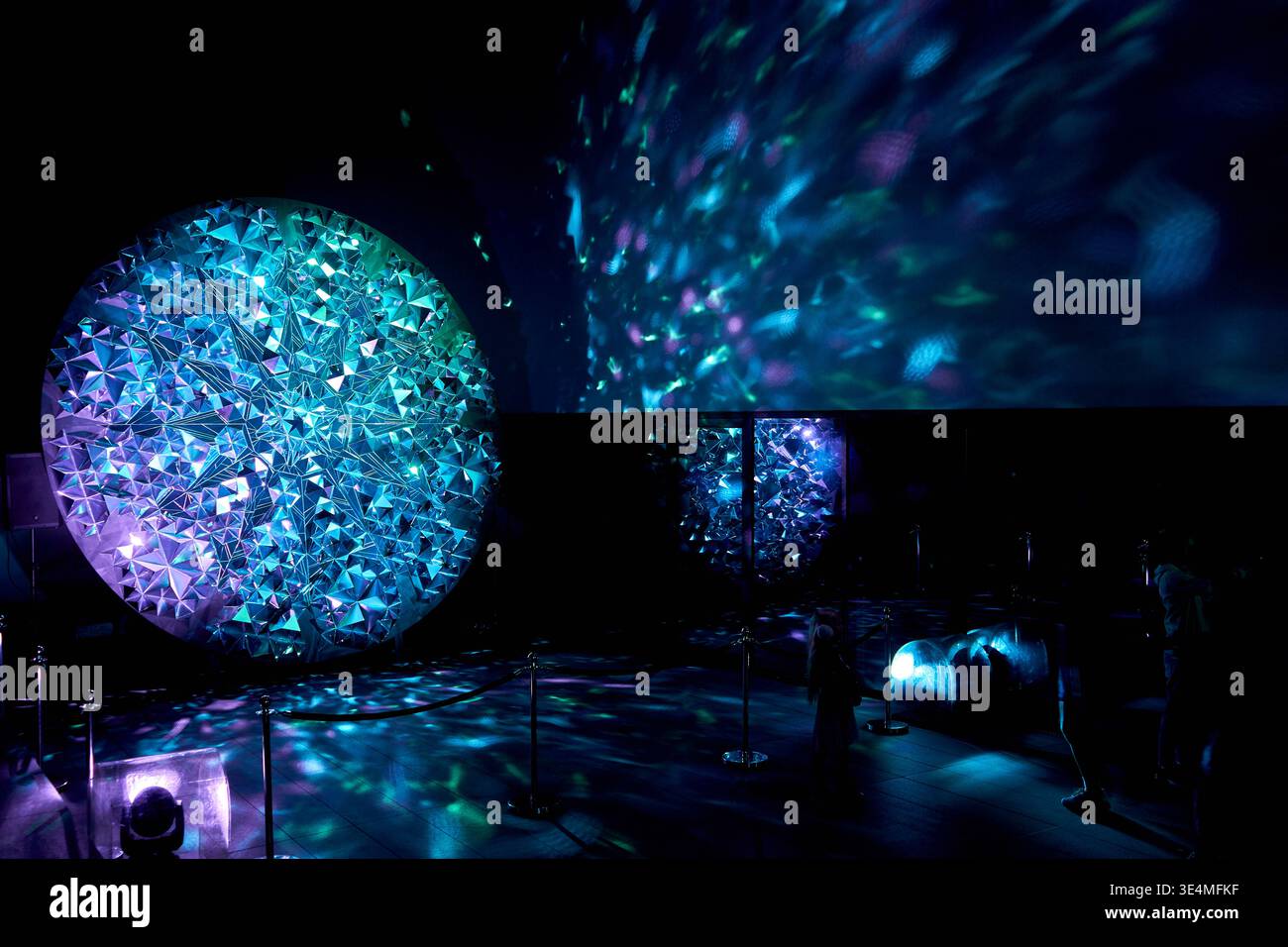 An immersive light art installation at a festival featuring a large circular structure covered in geometric triangular mirror pieces that reflect Stock Photo