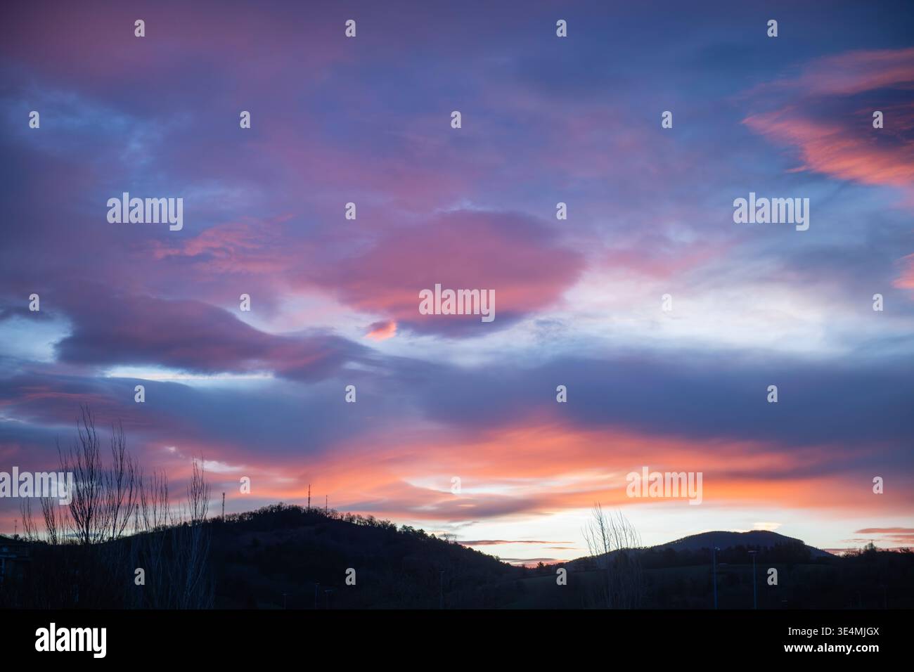 Colorful sunset with dramatic pink and blue clouds over a mountain horizon. Peaceful landscape with soft light and natural atmosphere, ideal for backg Stock Photo