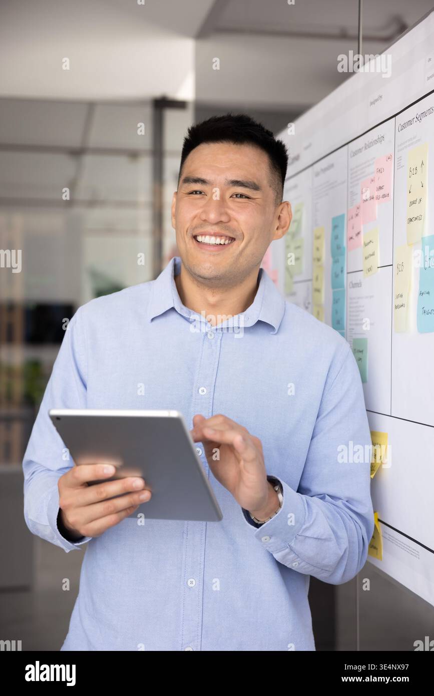Smiling young entrepreneur standing at planning board holding digital tablet Stock Photo