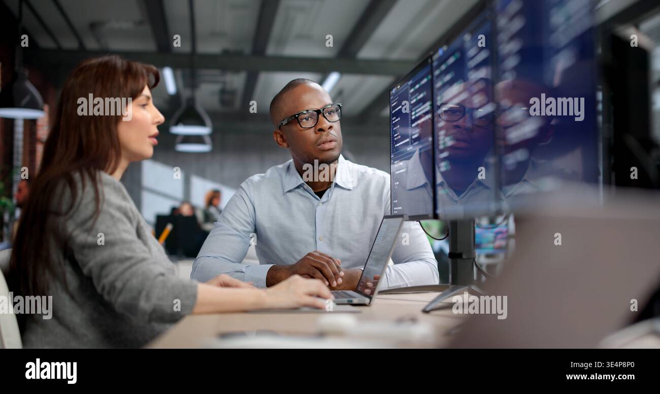 Young Female Coder And Male Software Developer Debug Code On Dual Desktop Monitors Stock Photo