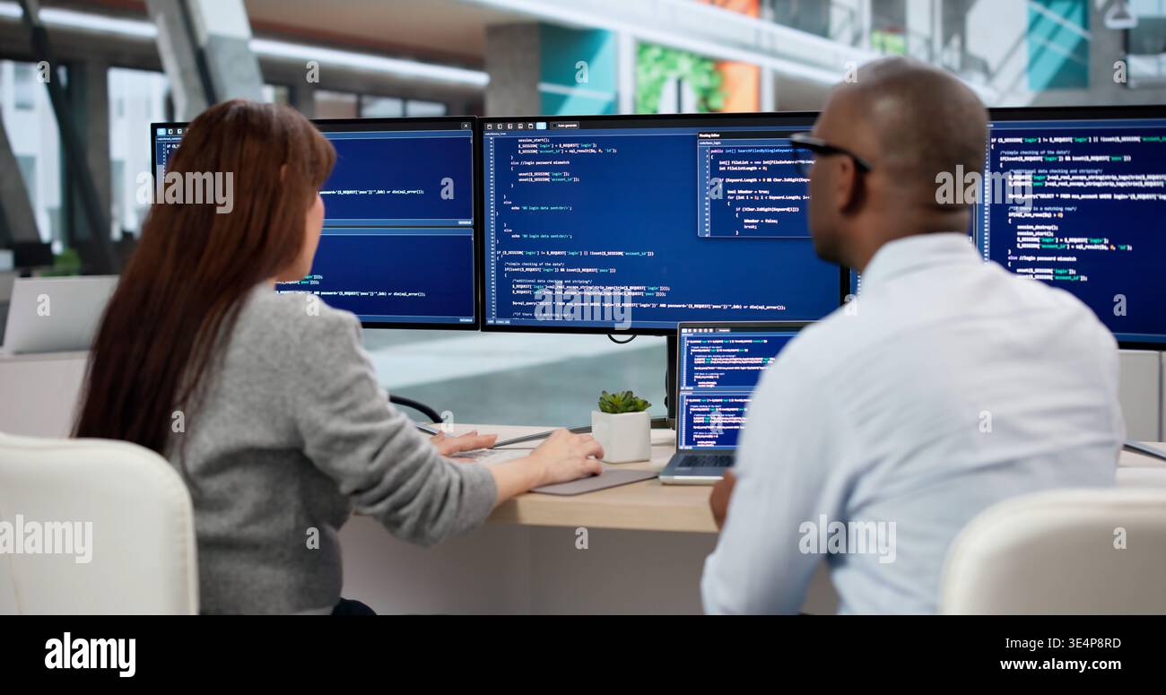 Two Young Software Developers Coding Together At Their Office Desk. Focused Engineers Analyzing Data Stock Photo