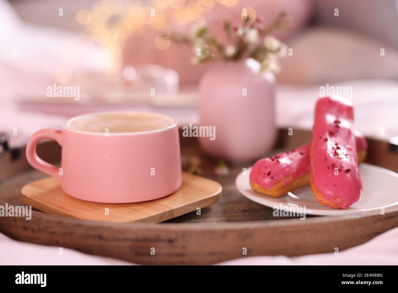 Aromatic coffee in cup, eclairs, and beautiful flowers on bed, closeup Stock Photo
